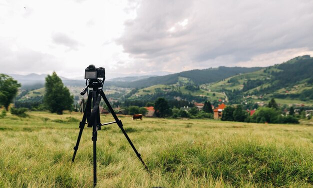 L'appareil photo sur un trépied capture un magnifique paysage de montagne avec un village et une forêt