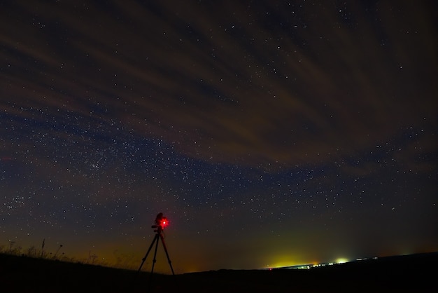L'appareil photo sur le trépied prend des photos d'étoiles de l'espace ouvert dans le ciel nocturne avec des nuages.