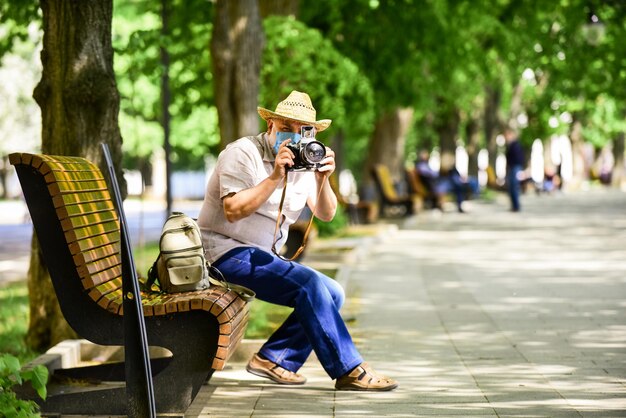 L'appareil photo à usage touristique prend une photo. Photographie urbaine. Homme senior en masque respiratoire. Le photographe professionnel travaille pendant la quarantaine du coronavirus. Notion de pandémie. Photographe risqué. Continue de travailler.