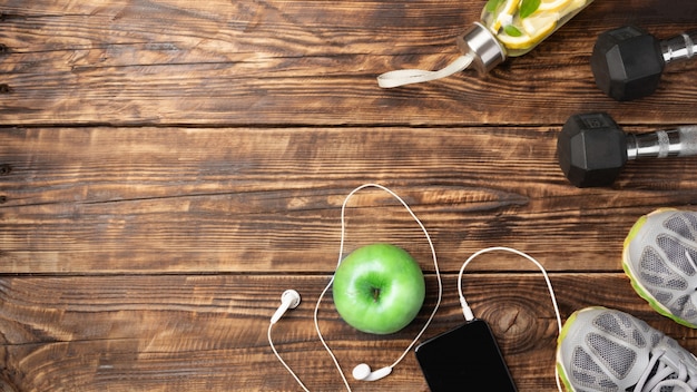 Appareils de fitness sur fond en bois avec espace copie: haltères, téléphone avec casque, pomme verte, baskets.