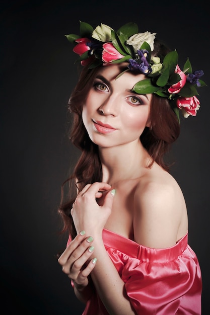 Apparence douce et romantique de la jeune fille avec une couronne de roses sur la tête et une robe rose. Joyeuse femme de printemps Jolly. Dame d'été en robe longue rose