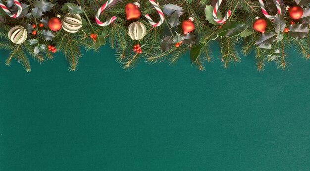 Appartement de Noël créatif posé sur du papier vert avec des décorations rouges, beaucoup d'espace de copie. Brindilles de sapin et de houx naturelles décorées de cannes de bonbon, de bibelots en verre et de fruits de lime secs.