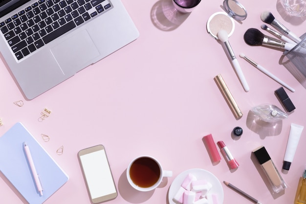 Appartement poser avec une tasse de thé ou de café, un ordinateur portable ou un ordinateur, femme composent des produits sur fond rose, vue d'en haut.