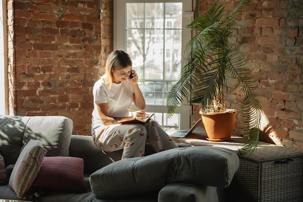 Appel des clients. Femme caucasienne, pigiste pendant le travail au bureau à domicile pendant la quarantaine. Jeune femme d'affaires à la maison, auto isolée. Utilisation de gadgets. Travail à distance, prévention de la propagation du coronavirus.