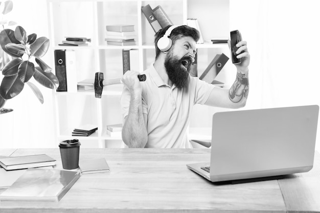 Appel entrant La chose la plus ennuyeuse à propos du travail dans un centre d'appel Client ennuyeux appelant Homme barbu écouteurs bureau swing marteau sur smartphone Communication gâtée Échec des négociations mobiles