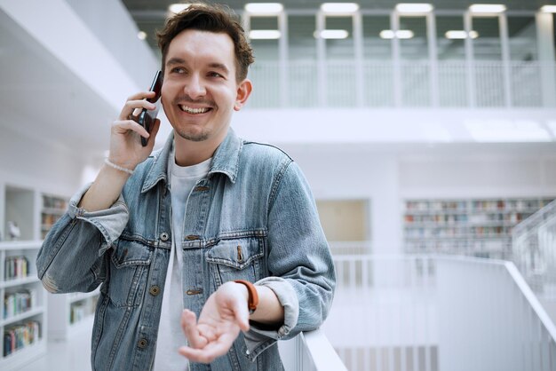 Appel téléphonique de l'homme et communication à la bibliothèque pour une conversation ou des conseils Heureux homme souriant parlant sur un smartphone mobile dans une grande librairie ou étudiant pour prendre une décision, un choix ou une idée