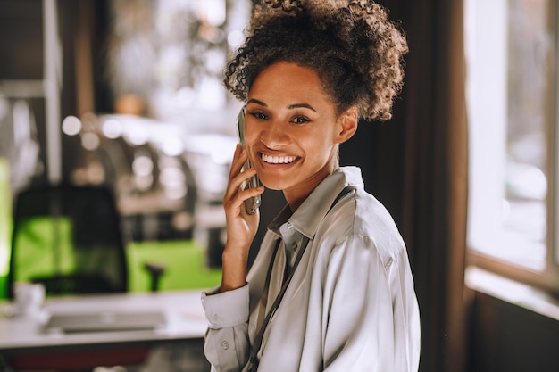 Appel téléphonique. Jolie femme souriante à la peau foncée parlant au téléphone