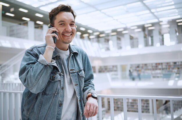 Appel téléphonique et portrait d'un homme pour une conversation heureuse dans un bâtiment de bibliothèque avec un état d'esprit positif Jeune personne ou étudiant de la génération z avec un smartphone pour la communication, la conversation et le bonheur