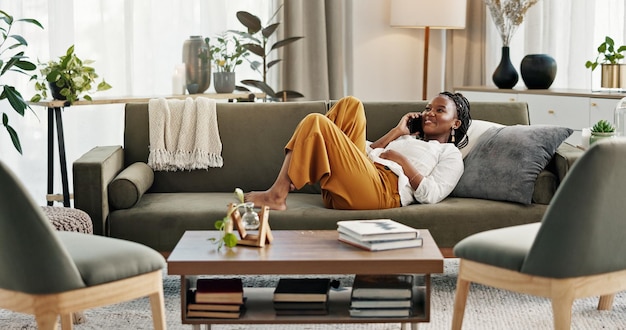 Photo appel téléphonique rire et femme noire sur le canapé pour parler conversation drôle et discussion en ligne la communication de réseau et la personne se détendre sur le smartphone avec l'humour blague et la comédie chat à la maison