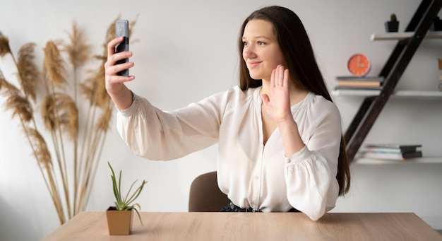 Appel vidéo au téléphone adolescente agitant la main en parlant avec l'enseignant ou des amis sur les réseaux sociaux Communication vidéo étudiante Numérique et mobile Un gadget pour la communication et la dépendance