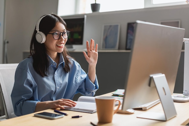 Appel vidéo femme japonaise agitant la main à l'ordinateur au bureau