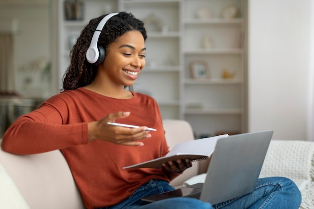 Appel vidéo d'une femme noire souriante portant des écouteurs en téléconférence sur un ordinateur portable à la maison