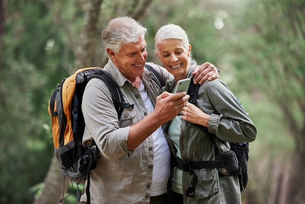 Appel vidéo téléphonique et couple de personnes âgées en randonnée dans une forêt heureux et souriant tout en se liant à l'aventure Personnes âgées actives en ligne et cartes pour homme et femme faisant de la randonnée dans la nature tout en vérifiant l'emplacement