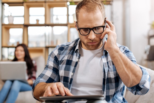 Appelez pour affaires. Homme indépendant sérieux et confiant tenant un téléphone portable et passer un appel tout en travaillant sur la tablette