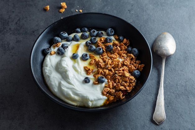 Appétissant muesli maison avec baies et yaourt servi dans un bol sur fond sombre.