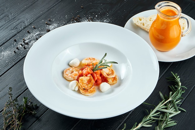 Appétissante soupe de tomate espagnole aux crevettes et mozzarella dans une assiette blanche sur bois noir