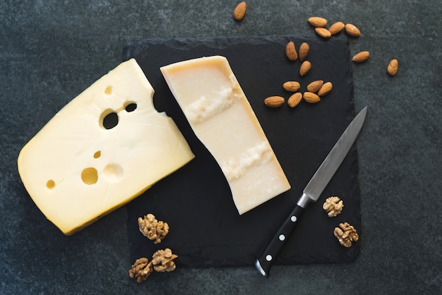 Appétissantes tranches de fromage solide sur une plaque noire avec un couteau, des amandes et des noix