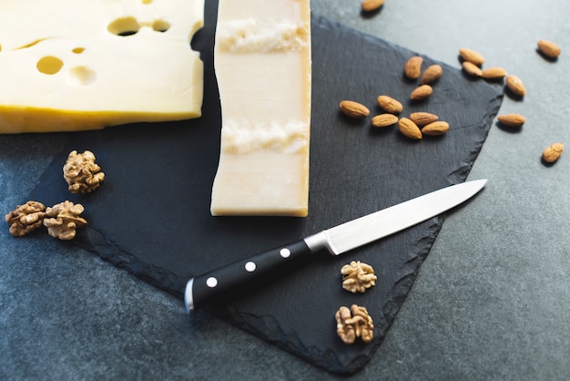 Appétissantes tranches de fromage solide sur une plaque noire avec un couteau, des amandes et des noix