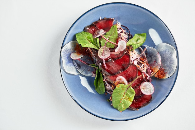 Photo appétit italien traditionnel bresaola bœuf séché sur des feuilles de laitue dans une assiette sombre sur une lumière