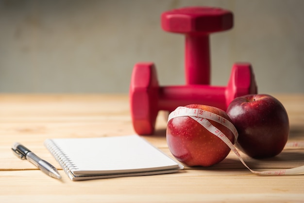 Apple, ruban à mesurer et bloc-notes avec des haltères allongé sur une table en bois