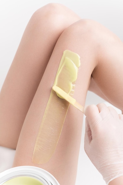 Application de cire chaude sur une jambe de femme mince à l'aide d'une spatule Épilation professionnelle à la cire dans un salon de beauté