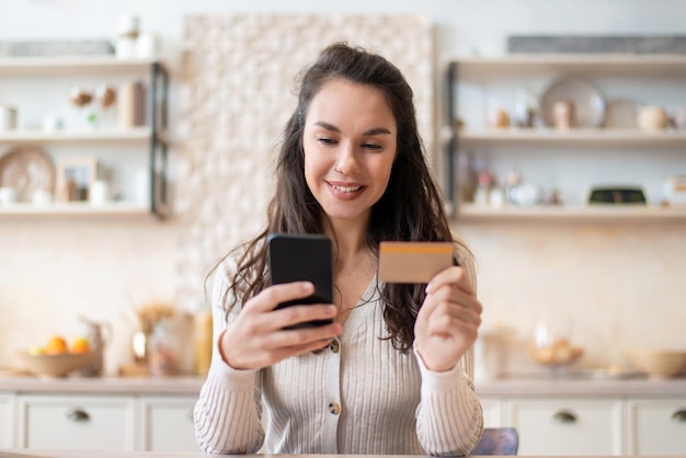 Application d'épicerie femme joyeuse utilisant une carte de crédit et un téléphone portable pour acheter de la nourriture en ligne en position assise