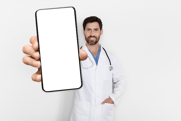 Application médicale beau médecin masculin en uniforme démontrant un grand smartphone vierge