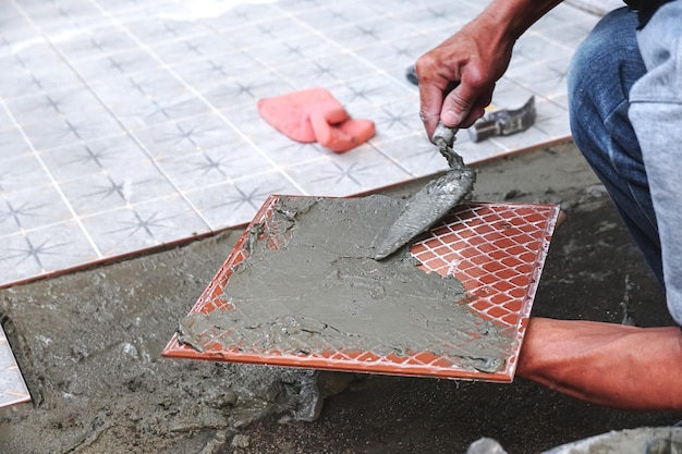 Application de mortier-colle sur un carreau. Appliquer l'adhésif, gros plan. Ouvrier plaçant des carreaux de sol en céramique