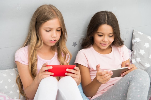 Application pour les enfants s'amusant à surfer sur Internet et à s'absenter de l'avis parental Accès Internet pour smartphone Les sœurs filles portent un pyjama occupé avec des smartphones Les enfants en pyjama interagissent avec des smartphones