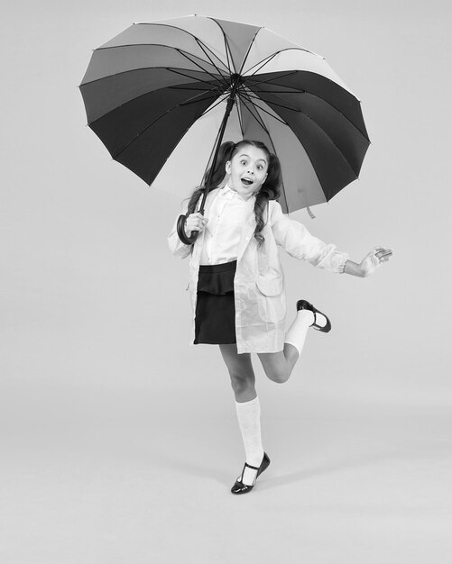 Application de prévision Concept de positivité Amusant jour de pluie Bonne promenade sous un parapluie Concept de pluie Enfant fille heureuse tenir un parapluie arc-en-ciel coloré Vêtements pour temps pluvieux Bonne humeur Enfant souriant