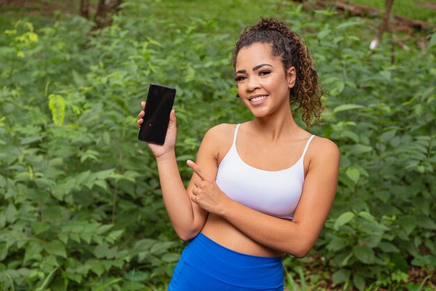 Application de sport. Portrait d'un jeune homme excité tenant et montrant un smartphone, pointant et indiquant un écran vide pour le texte. Extérieur