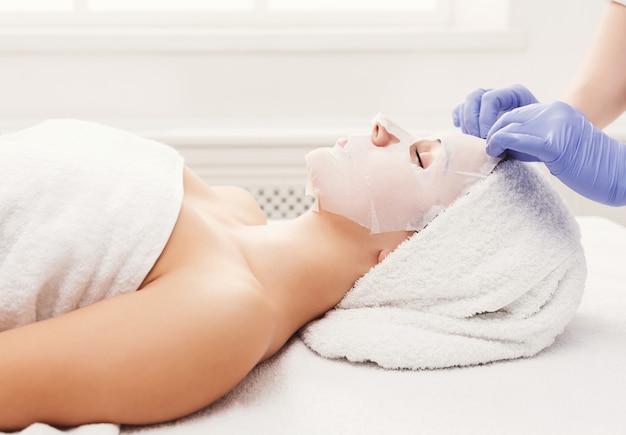 Appliquez un masque facial, un traitement de beauté spa et des soins de la peau. Femme obtenant un masque nourrissant pour le visage par une esthéticienne au salon de spa, gros plan, vue latérale