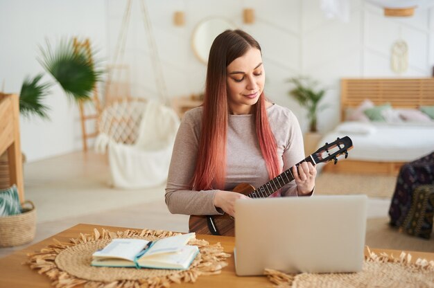 Apprendre en ligne à jouer d'un instrument de musique. Jeune femme apprenant à jouer du ukulélé à distance.