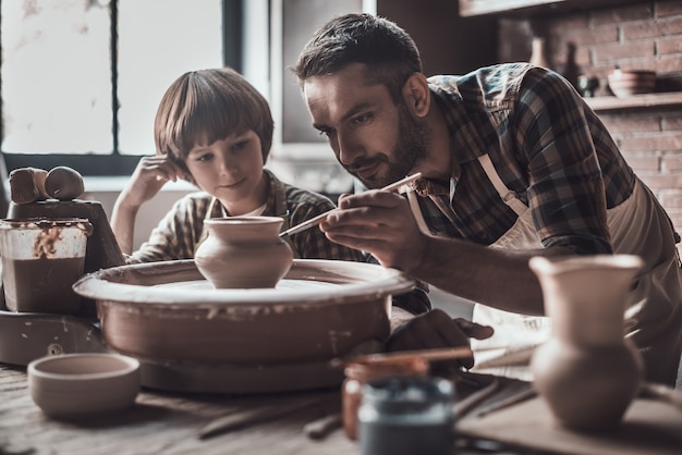 Apprendre de nouvelles compétences. Petit garçon regardant confiant jeune homme s'appuyant sur un pot en céramique à la classe de poterie