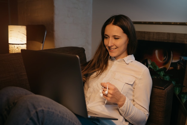 Apprentissage à distance. Une femme de race blanche avec un casque étudie à distance sur son ordinateur portable. Une fille heureuse sourit sur le canapé. Éducation à domicile.