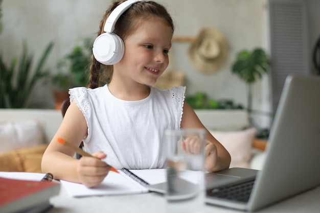 Apprentissage à distance. Joyeuse petite fille dans les écouteurs utilisant un ordinateur portable étudiant via un système d'apprentissage en ligne.