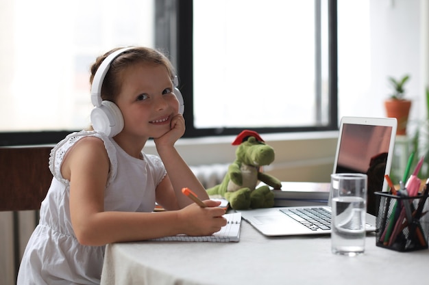 Apprentissage à distance. Joyeuse petite fille dans les écouteurs utilisant un ordinateur portable étudiant via un système d'apprentissage en ligne.