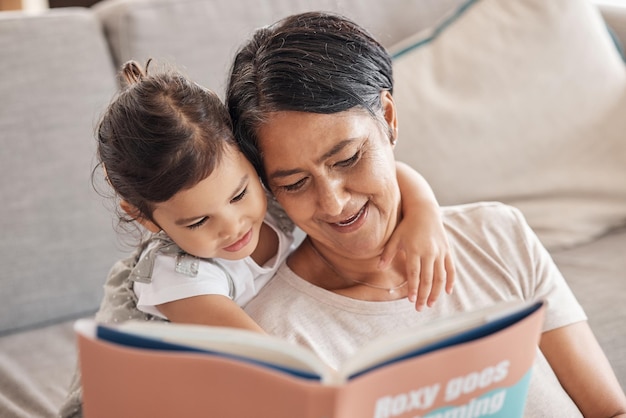 Apprentissage de l'éducation et fille et grand-mère lisant un livre sur un canapé se détendre et créer des liens dans le salon Les enfants aiment et racontent des histoires par une femme âgée appréciant une histoire fantastique avec un petit-enfant curieux