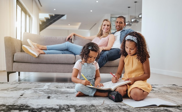 Apprentissage de la famille et des enfants dessinant dans le salon avec des parents sur un canapé Éducation artistique et filles créatives assises sur le sol tout en dessinant dans un livre de coloriage étudiant et se liant ensemble dans la maison