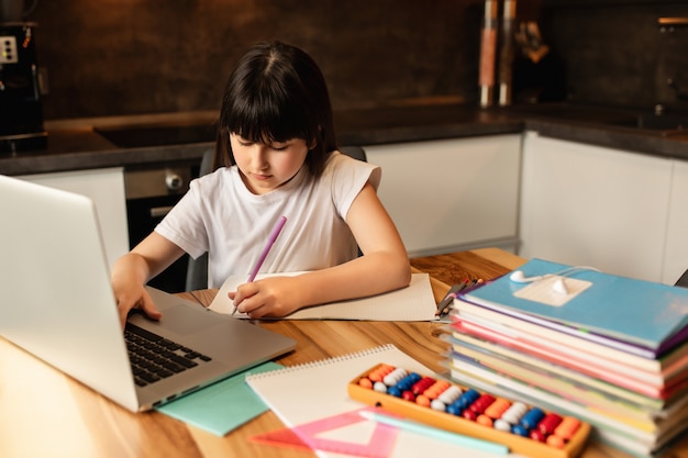 Apprentissage en ligne à domicile. Écolière avec un ordinateur portable fait ses devoirs. Enseignement à distance pendant la quarantaine