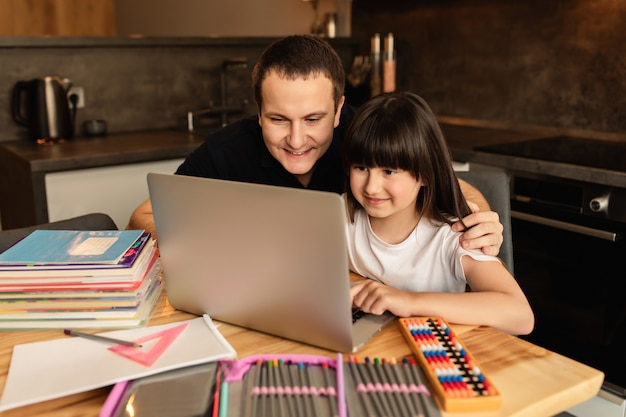 Apprentissage en ligne. Unité familiale tout en faisant ses devoirs. Un père aide sa fille à faire un cours en ligne à la maison