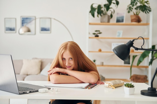 Appuyé sur la table Une adolescente aux cheveux blonds est à la maison pendant la journée