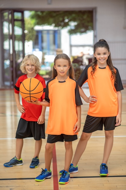 Photo après un bon match. enfants en tenue de sport debout avec un ballon et l'air satisfait