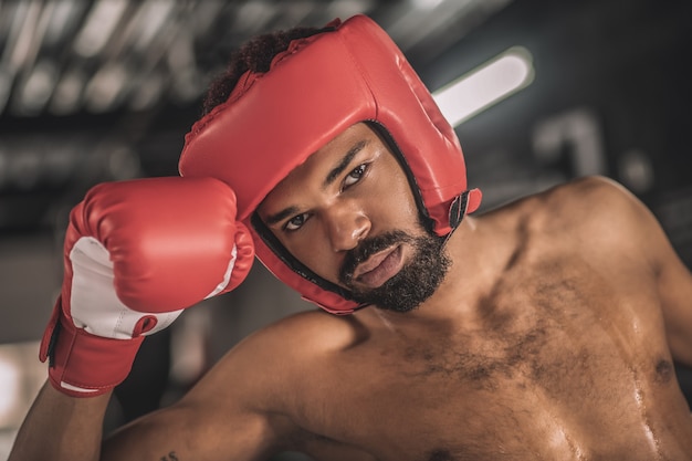 Après le combat. Kickboxer à la peau foncée dans un hemlet rouge semblant fatigué après le combat