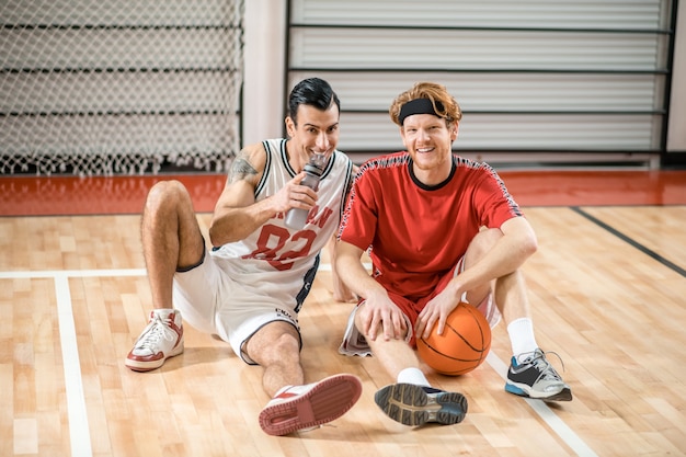 Après le jeu. Deux amis assis sur le sol dans la salle de sport et se reposant après le match