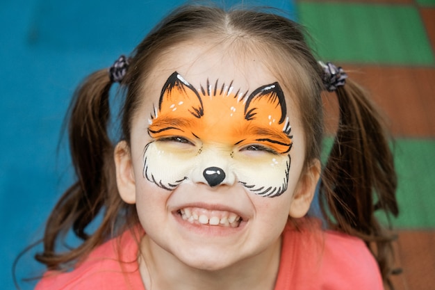 Photo aquagrim sur le visage de l'enfant. portrait d'une jeune fille avec un motif de chanterelles sur son visage. animation pour les vacances. tatouage pour un jeune enfant. la créativité des enfants.