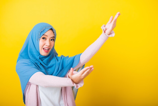 Arabe musulman asiatique, Portrait d'une belle jeune femme heureuse Islam religieux porter voile hijab sourire drôle elle ouvre les bras pour un câlin ou lève la main pour ramasser des objets recevoir quelque chose d'en haut isolé jaune