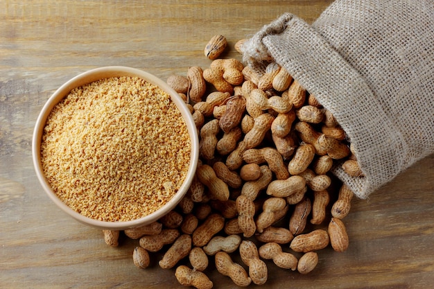 Arachides broyées et moulues dans un bol en céramique formant de la farine sur des aliments biologiques de table en bois rustique