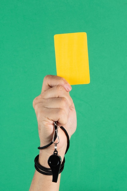 Arbitres main tenant un carton jaune et sifflet sur fond vert.