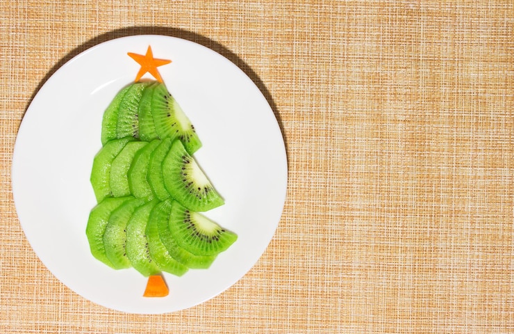 Photo arbre comestible de noël fait de kiwi et de carotte sur une assiette sur la table. idée de dessert pour les enfants. concept d'art culinaire du nouvel an. vue de dessus, copiez l'espace. photo de haute qualité